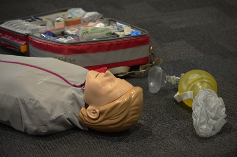 A CPR training manikin lies on the floor next to a resuscitator bag and an open medical kit, ready for CPR and First Aid Training in Peregian Springs.